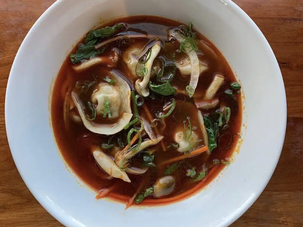 A bowl of wonton soup featuring yen tsai (pickled vegetables) from Hop Alley