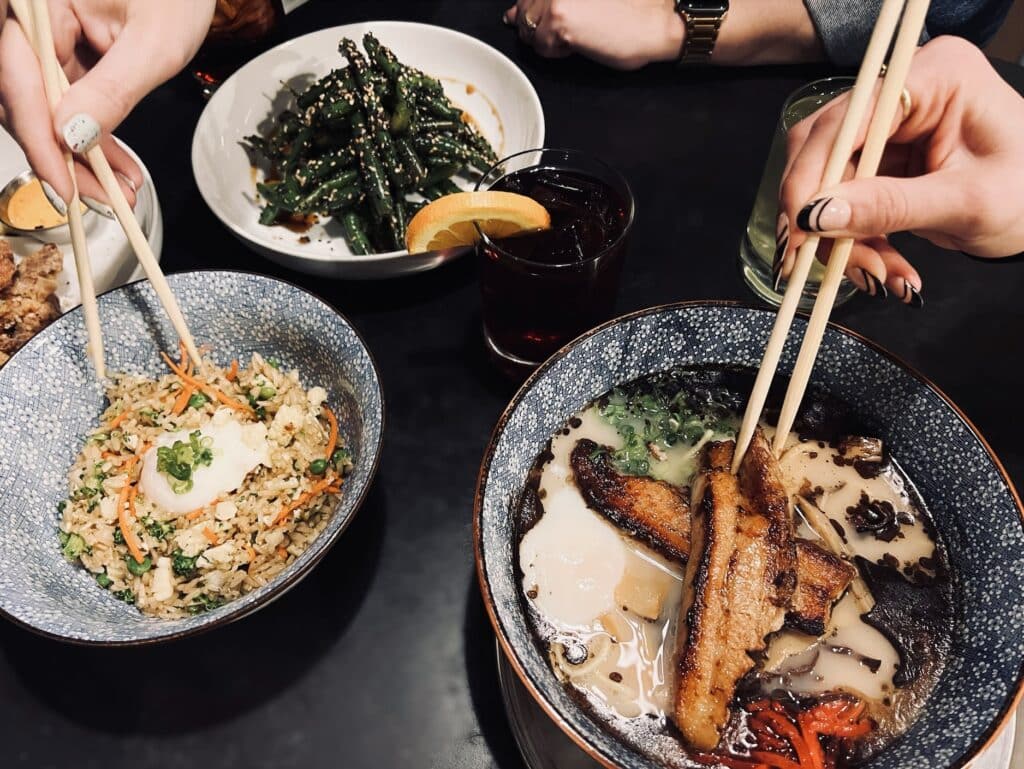 Two individuals using chopsticks to eat dishes by Osaka Ramen