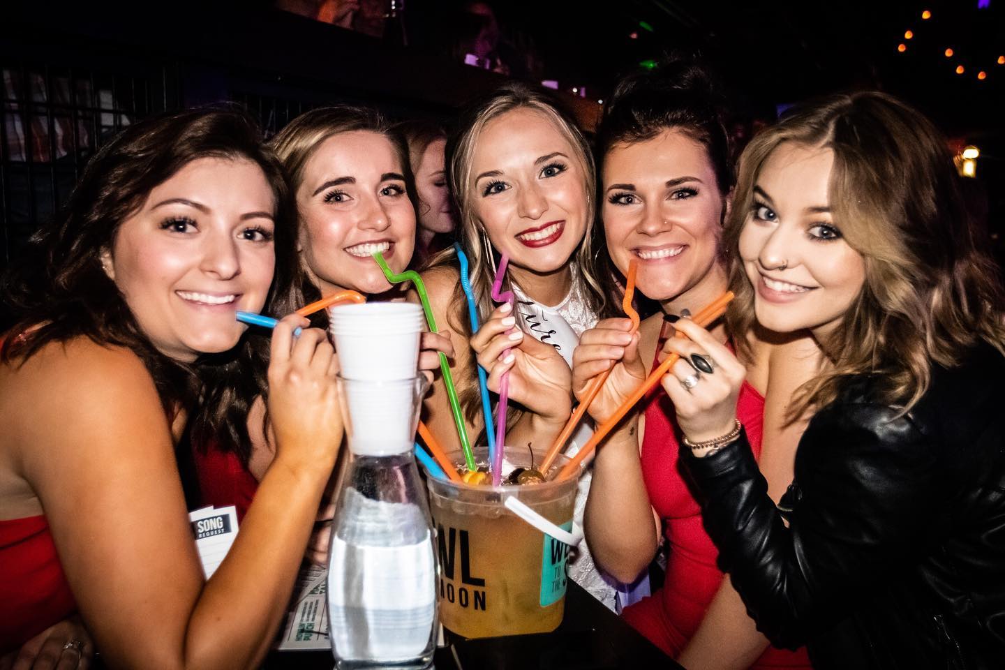 A group of women with straws sipping a bucket drink at Howl at the Moon