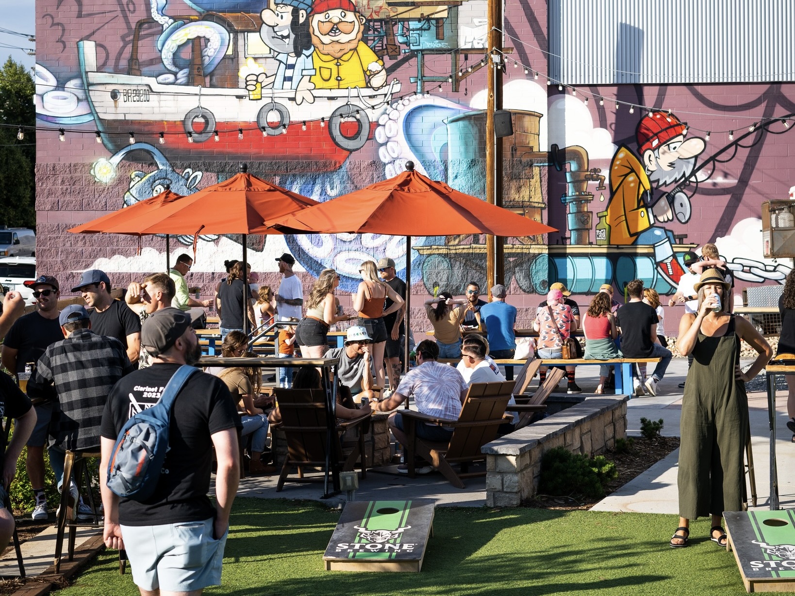 A group on Improper City's patio, featuring cornhole and a large mural