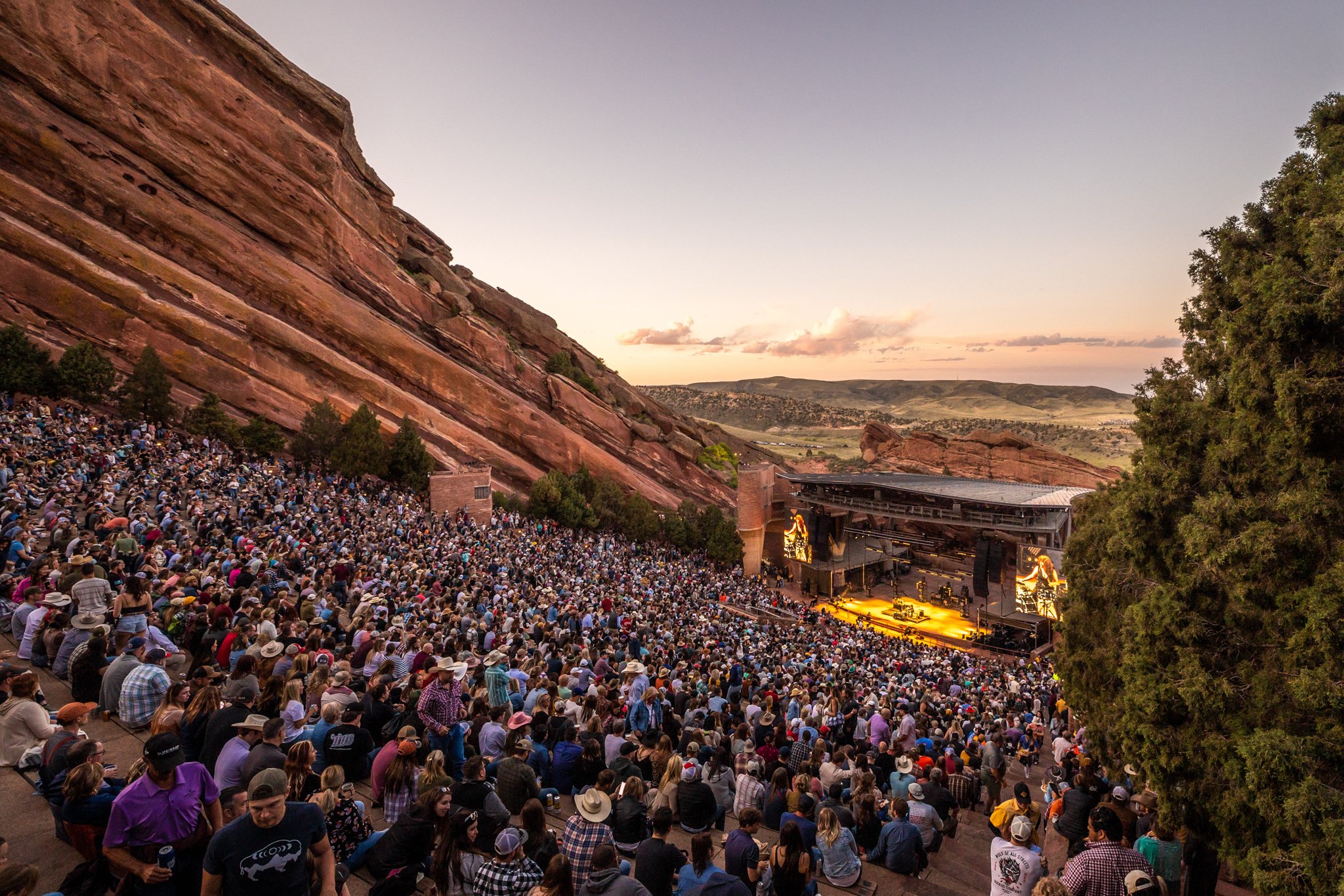 A crowd sitting at Red Rocks Amphitheatre watching the stage at sunset