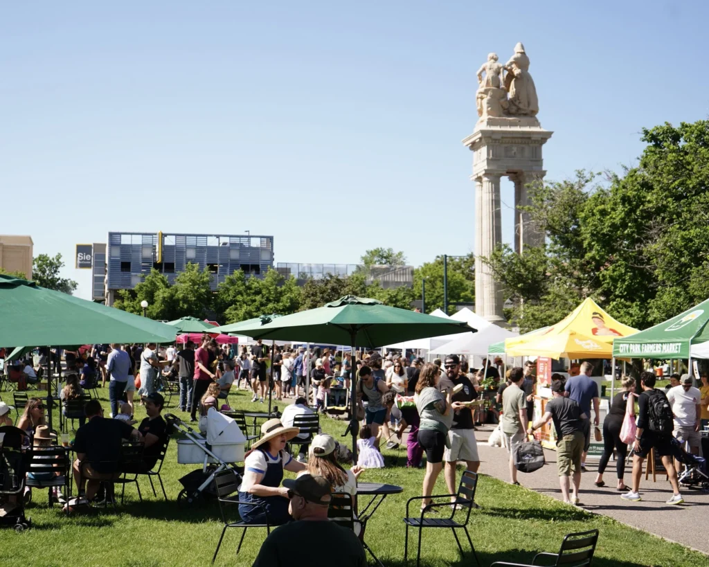 Crowds shopping and seated beneath shaded tables during the City Park Farmers Market