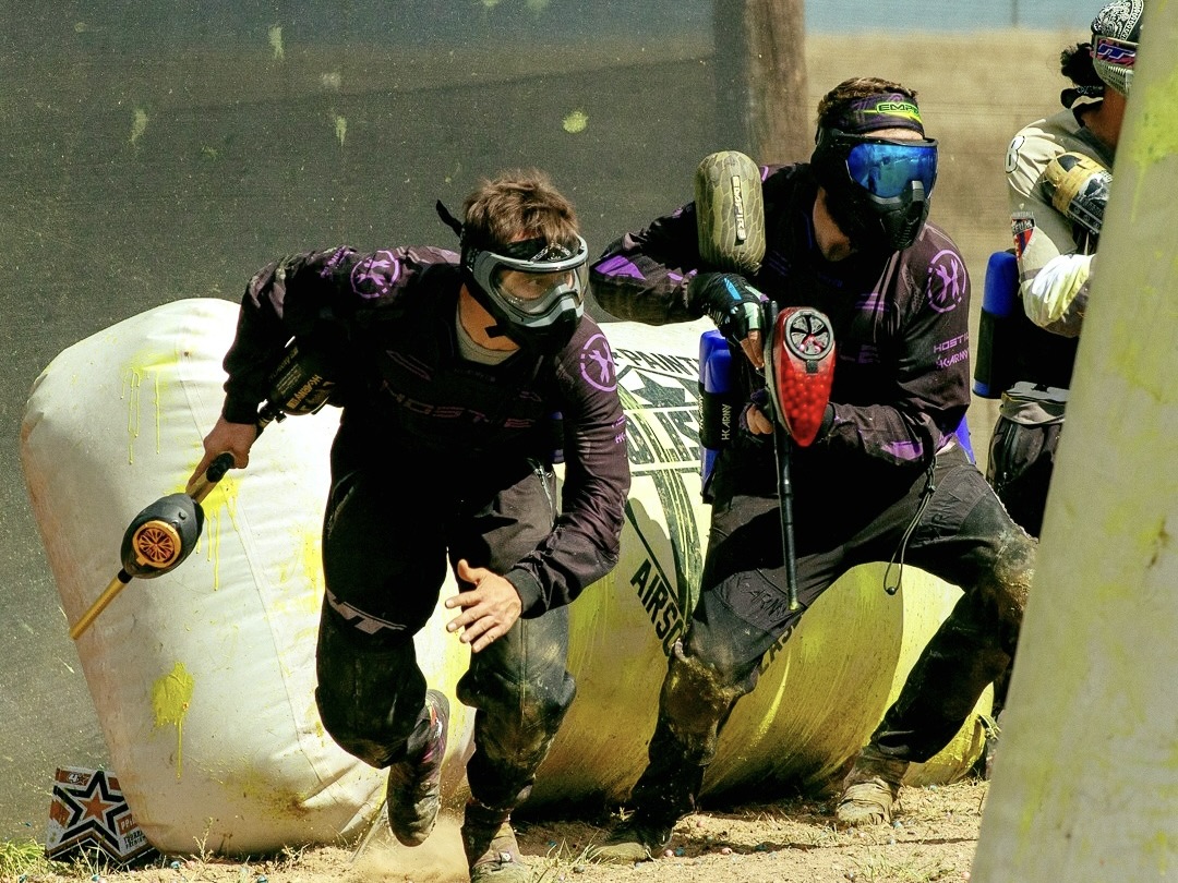 Three men in protective gear, hiding behind a barrier at American Paintball Coliseum