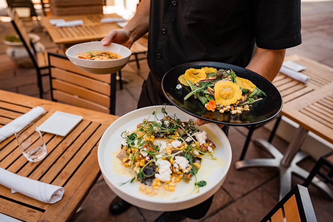 A server holding various seasonal dishes on the Rioja patio