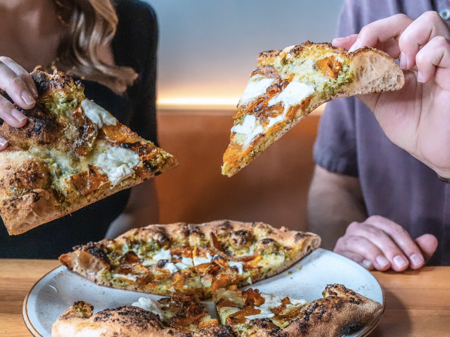 Two diners holding up slices of pizza from The Greenwich