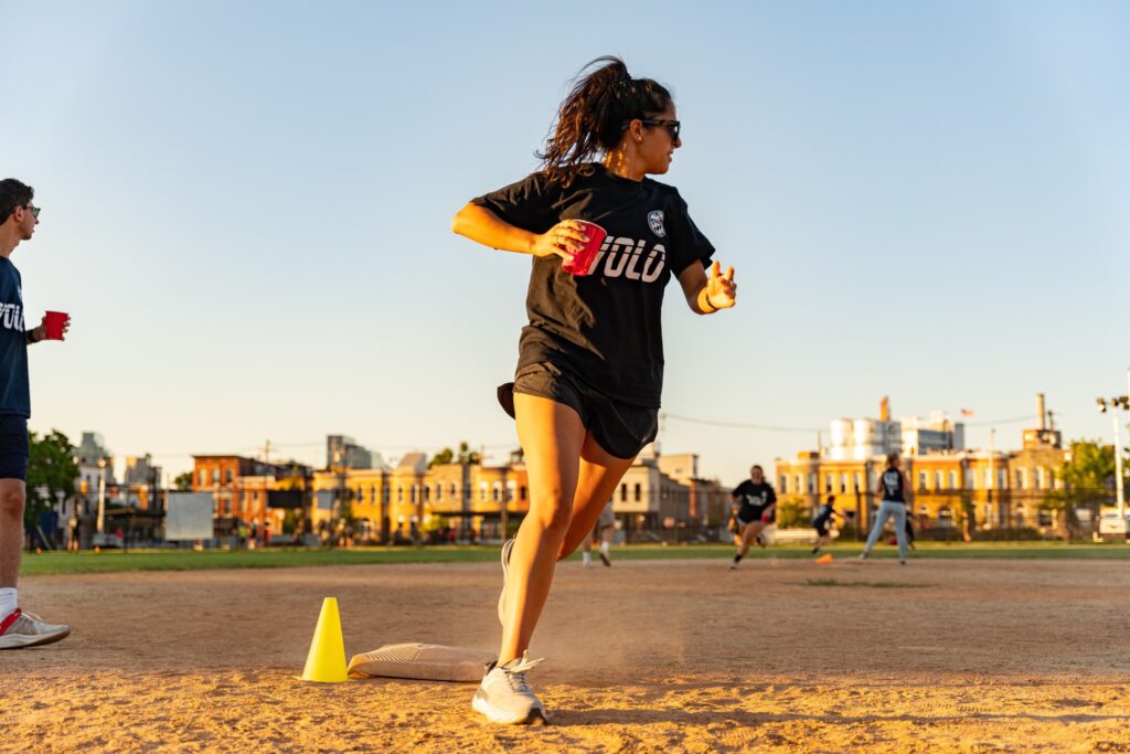 A woman holding a cup, running around a base during a kickball game