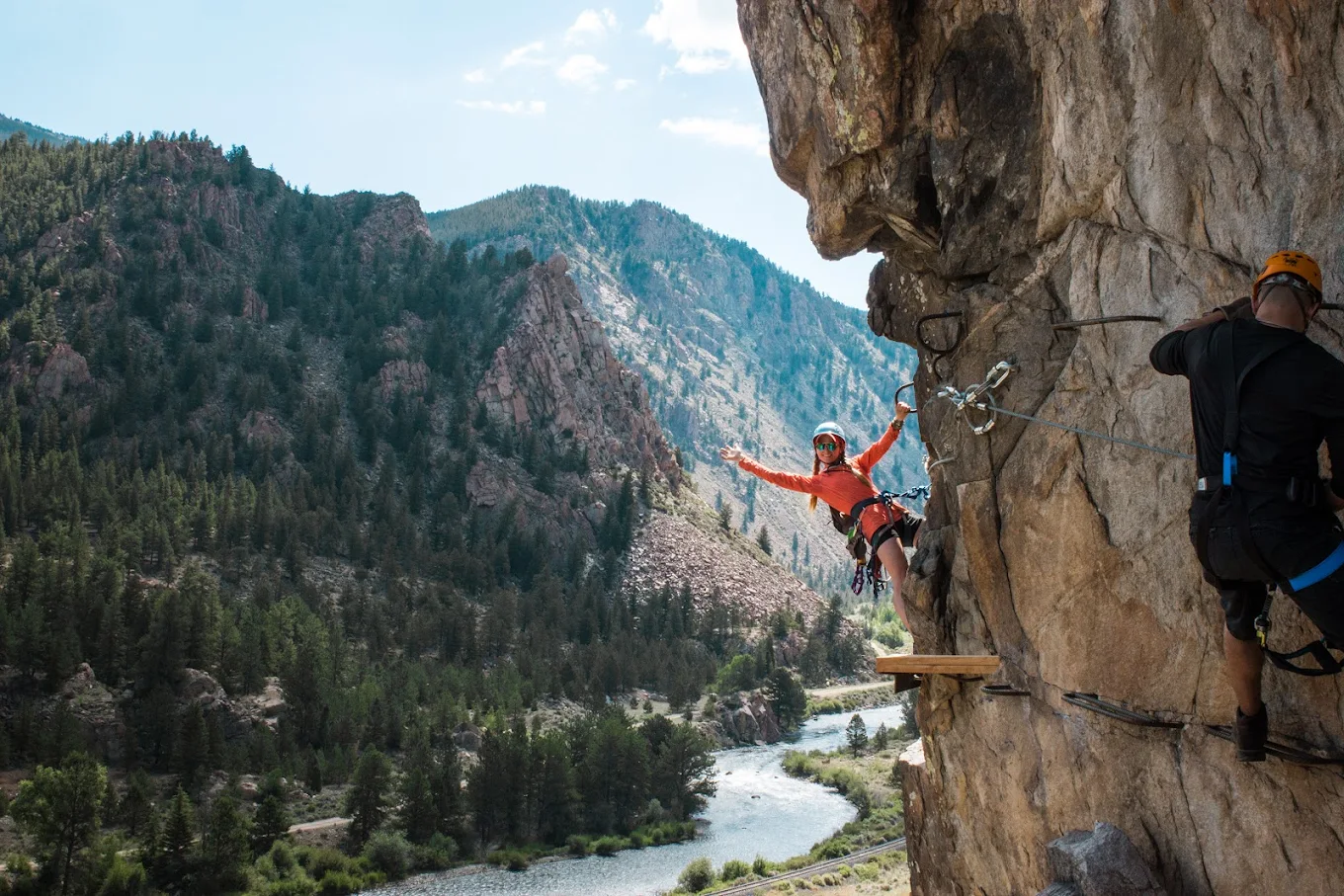A woman waving while hanging onto the Mount Blue Sky Via Ferrata